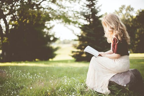 Young woman sitting on a rock reading her Bible A woman reads her bible while sitting on a rock outside. The outdoors can be a peaceful place to study God's Word.