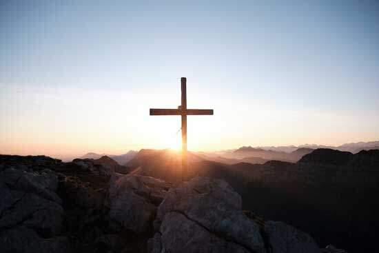A wooden cross stands on a mountaintop, illuminated by the sun.