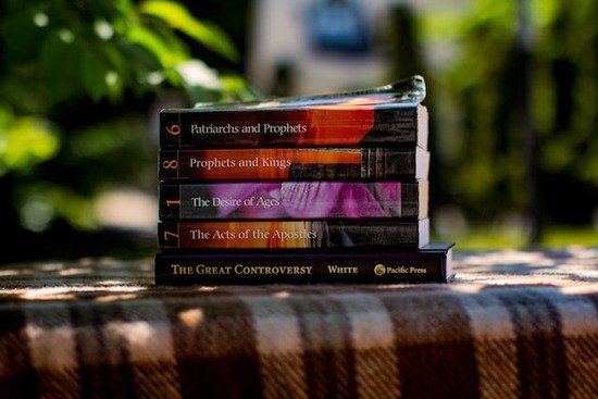 Conflict of the Ages series of books by Ellen G. White A stack of Ellen G. White's books sits on a blanket outdoors.