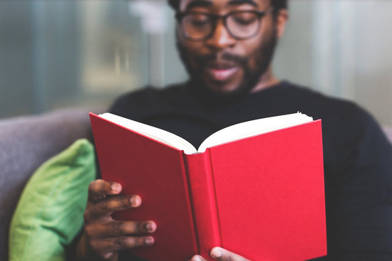 A man sitting on his living room couch reading a copy of Ellen White's writings.