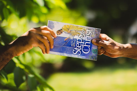 Someone handing out the book Steps to Christ as a way of sharing God's love