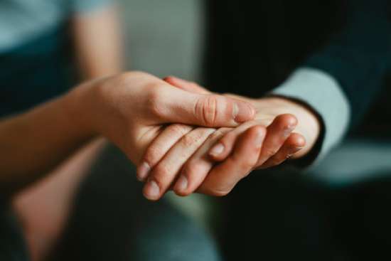 A hand holding another hand with humility, offering them support