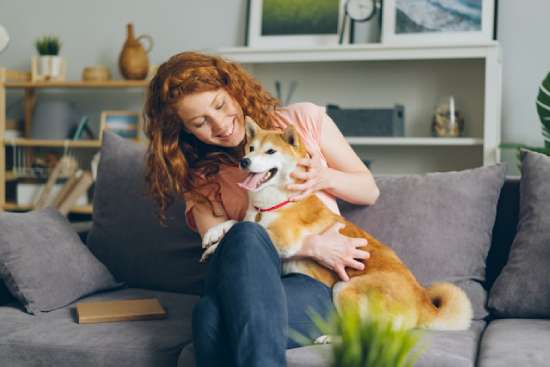 A kind woman holding her dog on a couch petting it