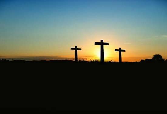 Three crosses stand near each other underneath a sunset sky.