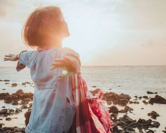 A woman standing on a beach, arms outstretched, symbolizing our free will