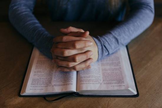 A man folding his hands in prayer over a Bible.