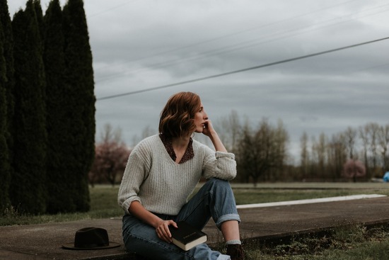 A women sitting on a sidewalk and holding a Bible as she contemplates its authority in her life