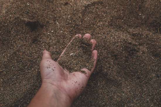 A hand sifting through sand representing the dust that was used to create humankind.