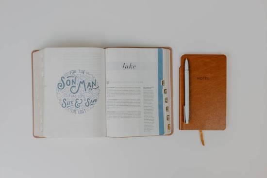 A Bible is open to the book of Luke and sits next to a notepad, illustrating the importance of studying the Bible to better understand the names of Jesus