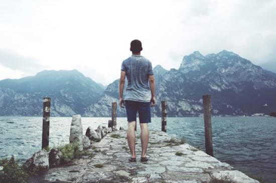 A man stands bravely on a stone pier facing the mountains. This illustrates how we can be courageous when facing spiritual warfare.