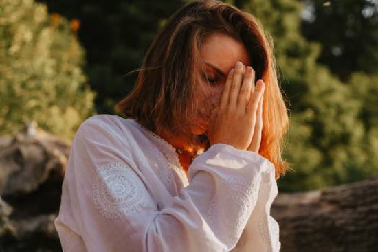 A woman prays with her hands folded and eyes closed, demonstrating how prayer can help overcome demonic powers.