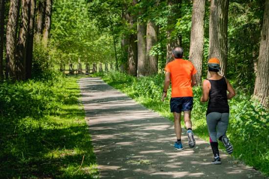 A man and woman running on a trail in a forest. Exercising outdoors can do wonders for our health!