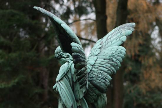 A green angel statue in a forest, illustrating the Adventist belief that the devil is a created angelic being.