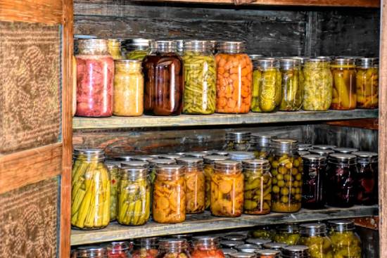 Canning jars full of preserved foods fill up shelves, illustrating how country living can enable us to grow and preserve our food and reduce the need to go to the store.