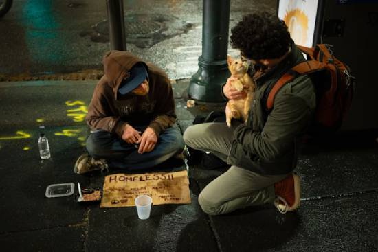 A man stoops by the curb to help a homeless person.