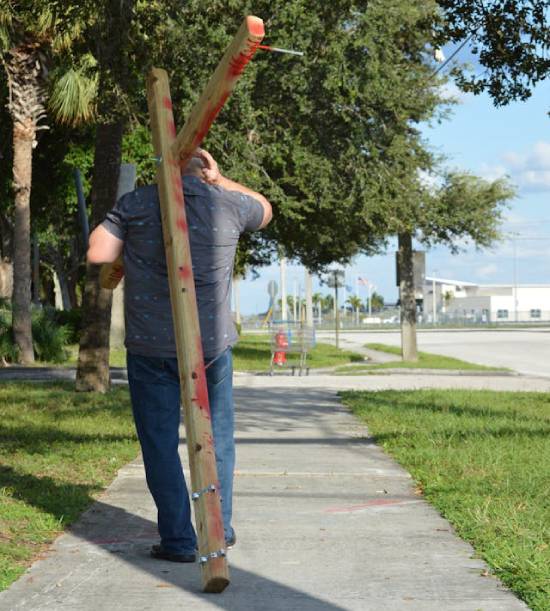A man carries a cross down a modern-day sidewalk, making us wonder what it really means to pick up your cross like Jesus.