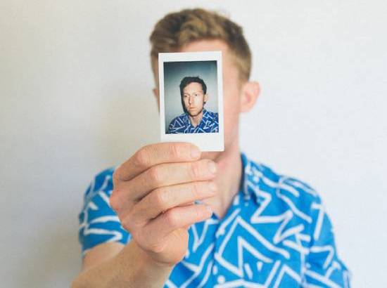  young man holds a headshot of himself in front of his own face.
