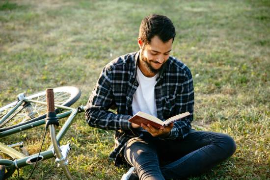 A man sits in a green field next to a bike while reading his Bible—a reminder that the Bible is our ultimate source of truth.