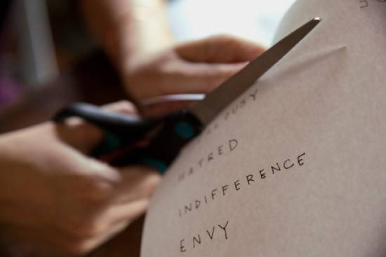 A person cuts out words of negative character traits (e.g. hatred, indifference, envy) from a piece of paper.