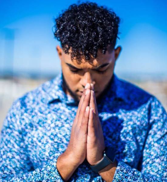 A young man bows his head in reverent prayer.