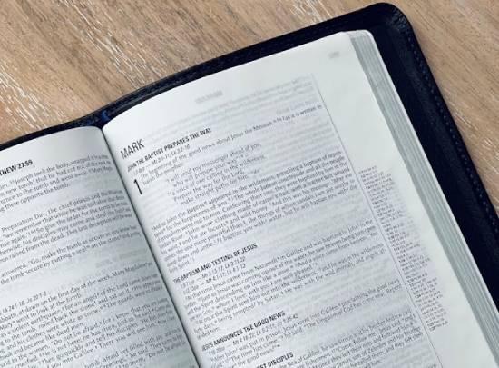 A black Bible lies open to the first page of the book of Mark.