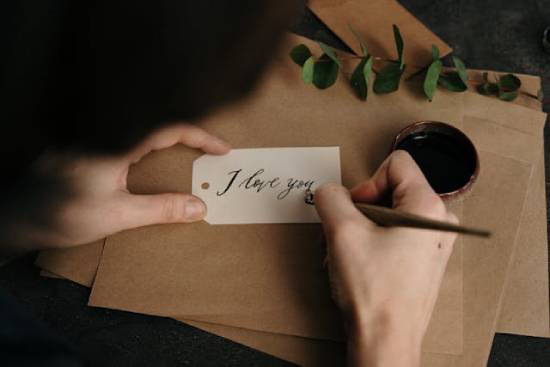 Someone writes 'I love you' in calligraphy on a handmade note.