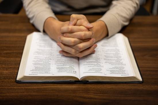 A person clasps their hands together on top of an open Bible, signifying prayer