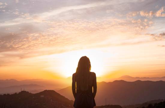 A woman watches the sunset from a mountaintop while contemplating the truth about life after death—something beautiful and reassuring when we understand what the Bible says.