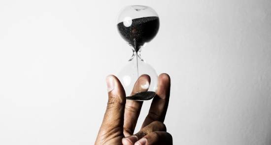 Someone holds an hourglass in the air, showing the ticking down of time.
