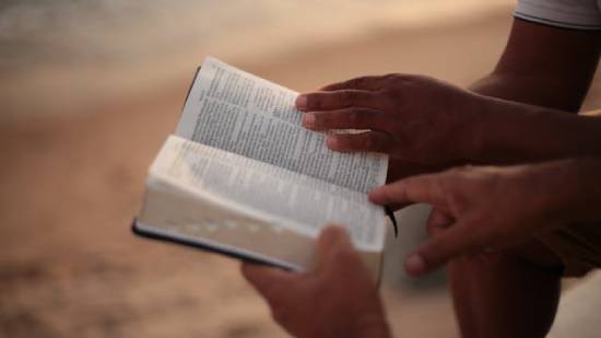 Two people reading a Bible on a beach.