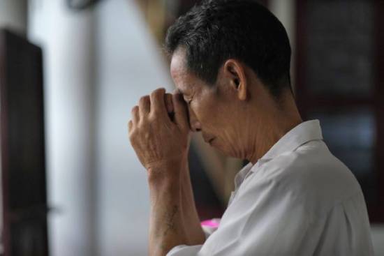 A man clasping his hands and closing his eyes in prayer