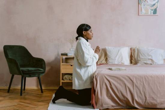 Woman kneeling beside her bed to pray an African American woman kneels at her bedside in prayer