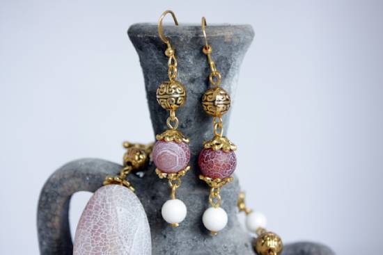 Two ornate earrings hang on the lip of a clay jar.
