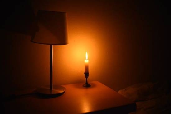Lit candle beside lamp The flame from a lit candle on a desk sits next to a dark lamp and lights the surrounding area.