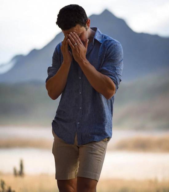 Man praying to God outdoors With a mountain in the distance as a backdrop, a young man prays with his head bowed.