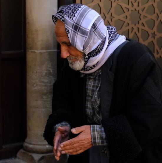 An elderly Jewish tax collector prays with his eyes closed and hands cupped.