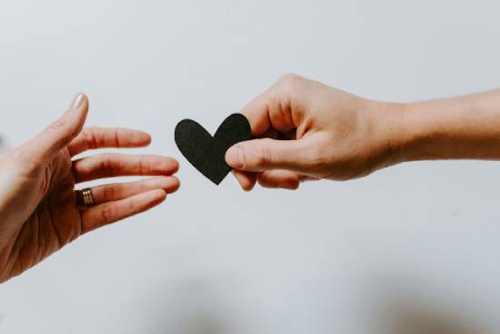 A hand reaches across to another person's hand to receive a paper heart
