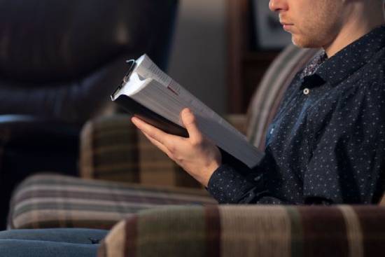 A man sits on a couch reading the Bible.
