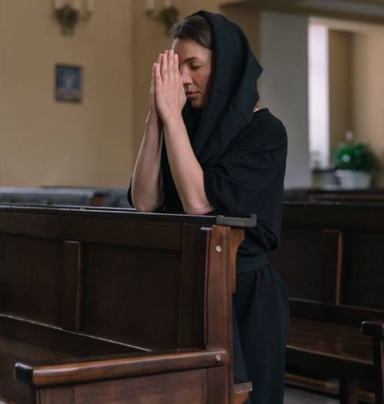 A woman in a head covering kneels and prays in a church.