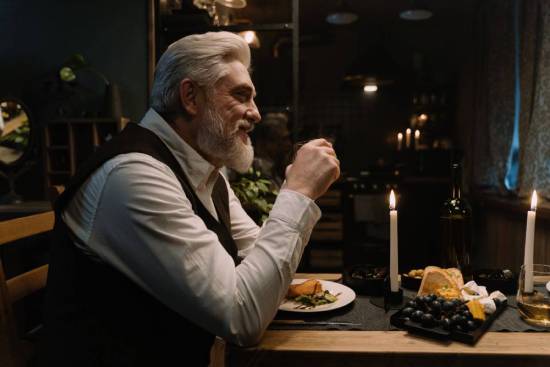 A well-dressed older gentleman sits at a fancy dinner table.