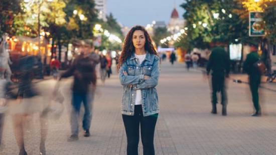 A woman stands in a courtyard in focus but those moving around her are out of focus.